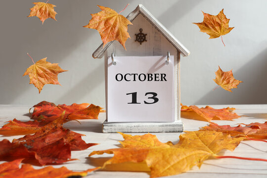 Calendar for October 13 : decorative house with numbers 13 and the name of the month in English, falling maple leaves , gray background, side view