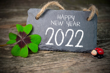Wooden hang tag and slate with four leaf clover and sparklers with happy new year 2022 on wooden...