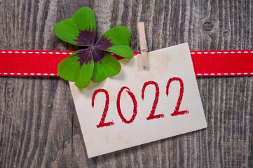 Wooden hang tag and slate with four leaf clover and sparklers with happy new year 2022 on wooden...