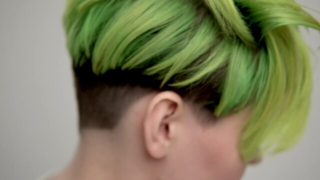 A young girl with a short pixie haircut and green hair in a white T-shirt on a light background. A woman poses in the studio, smiles and shows emotions. A breast portrait.