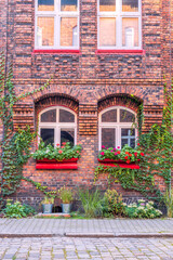 Fototapeta na wymiar Facade of an old, traditional, silesian brick block house in Nikiszowiec, Katowice, Poland. Small, colorful garden in front of the building.