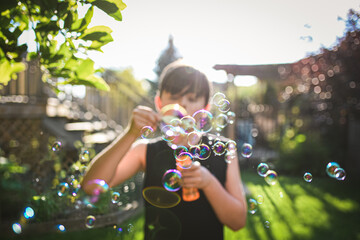 Young boy blowing bubbles in a backyard on a sunny day.