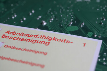 Viersen, Germany - May 9. 2021: Yellow certificate of work incapacity (german: Arbeitsunfähigkeitsbescheinigung) on green computer circuit board - obrazy, fototapety, plakaty