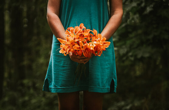 Cropped image of woman in blue dress holding bunch of orange flowers.