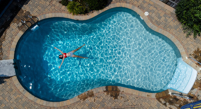 Overhead view of woman floating in a swimming pool on summer day.
