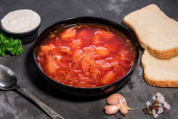 Borsch. Ukrainian soup. Red soup. Borsch with sour cream and onions, white bread. Traditional Russian borsch with sour cream. The concept of delicious food with sour cream on a black background