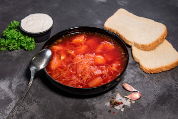 Borsch. Ukrainian soup. Red soup. Borsch with sour cream and onions, white bread. Traditional Russian borsch with sour cream. The concept of delicious food with sour cream on a black background