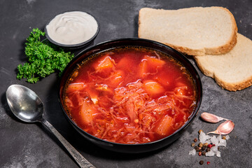 Borsch. Ukrainian soup. Red soup. Borsch with sour cream and onions, white bread. Traditional Russian borsch with sour cream. The concept of delicious food with sour cream on a black background