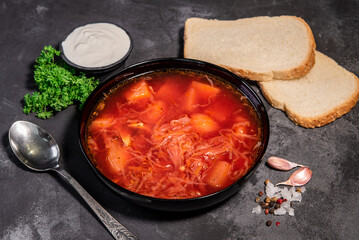Borsch. Ukrainian soup. Red soup. Borsch with sour cream and onions, white bread. Traditional Russian borsch with sour cream. The concept of delicious food with sour cream on a black background