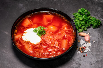 Borsch. Ukrainian soup. Red soup. Borsch with sour cream and onions, white bread. Traditional Russian borsch with sour cream. The concept of delicious food with sour cream on a black background