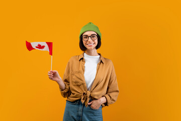Modern foreign education concept. Happy female exchange student holding small flag of Canada,...