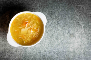 Chicken soup with noodles, potatoes, onions and carrots in a white deep plate on a gray background. Place for your text.