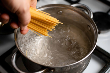 Boiling water in a saucepan and spaghetti in hand. Pasta cooking.