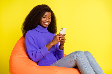 Photo of lady sit beanbag hold phone texting wear purple pullover jeans isolated yellow color background