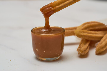 Traditional churros with sugar and cinnamon served on a marble table, with a bowl of caramel.