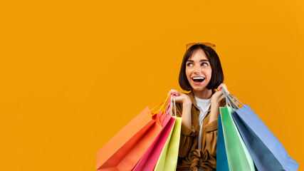 Fototapeta na wymiar Excited lady with shopping bags smiling and looking at free space, offering place for your ad over yellow background