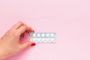 Woman's hand holds a pack of pills on a pink background, close-up. Women's health and medicine concept.