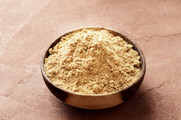 Wooden bowl full of dry ginger on textured background