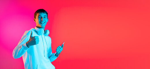 Flyer with young man, student or boy in casual clothes smiling isolated on magenta studio backgroud in neon. Human emotions concept.