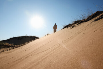 Fototapeta na wymiar Man in arabic clothes walking through desert on sunny day, back view