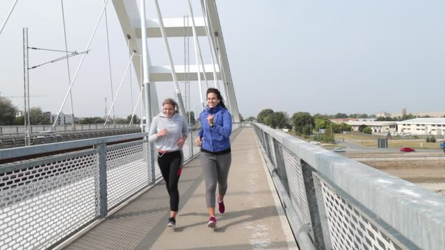 Two young happy and self loved woman the best friends jogging and running outdoor on the bridge for health life doing bodyweight workout and training by jog together while they listening to music 