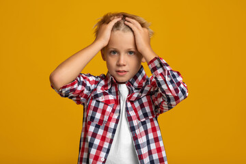 Upset sad surprised caucasian teenage boy presses hands to his head, isolated on yellow background