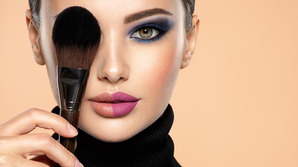 Portrait of a girl with cosmetic brush at face. Woman covering one eye on the face using makeup...