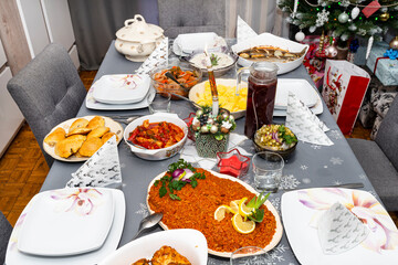 A table set before the supper for Christmas in Poland, visible baked fish fillets in a carrot salad, a holy wafer and dumplings.