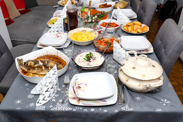 A table set before the supper for Christmas in Poland, visible baked fish fillets in a carrot salad, a holy wafer and dumplings.