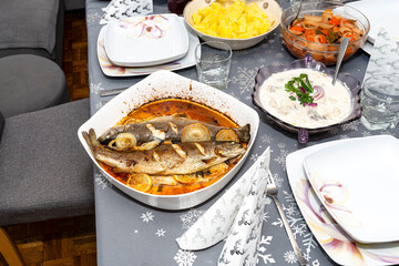 Baked two pieces of trout on a plate with onions and lemon slices dipped in oil on the holiday Polish table.