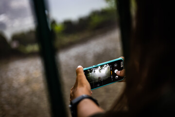 Rear view of a young woman making picture on phone camera while enjoying her vacation holidays in the rainy forest, girl photographing amazing landscape on her smart phone
