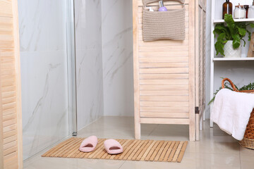 Wooden mat with slippers on floor in bathroom