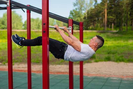 Caucasian man doing a back plank on the uneven bars. Workout on the sports ground.