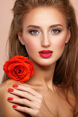 Fototapeta na wymiar Beautiful young woman with a red flower in hand near face. Portrait of a girl with red rose in hands