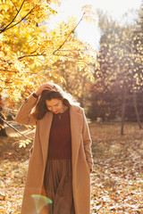 Beautiful woman in beige coat and red lips walking in autumn park with gorgeous natural light