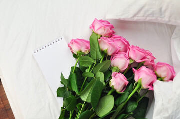 Bouquet of pink roses on the white linens on bed 