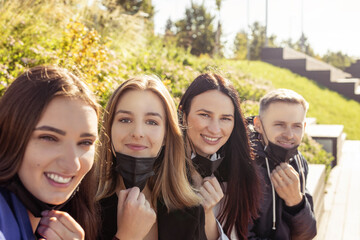 Group of young and attractive friends taking selfie with taking off black medicine faces masks during coronavirus outbreak. Bright vivid backlight filter. Second from left woman is in camera focus