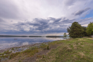Evening landscape on the lake in early spring. The dramatic sky is reflected in the water.