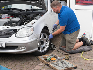 A male mechanic prepares to undo the wheel nuts on a silver sports car with a long handled...