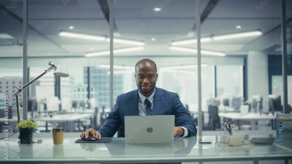 Poster successful black businessman in tailored suit working on laptop computer on top floor office overloo
