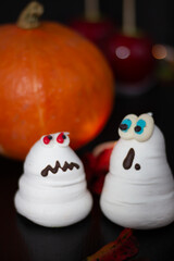 Engaging duo of meringue specters, one startled and the other perturbed, stand proudly beside a fresh Halloween pumpkin.