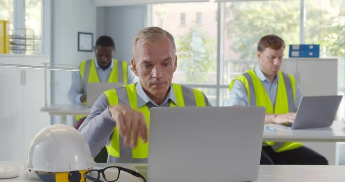 Portrait of tired industrial architect working on laptop in office