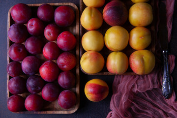 Yellow nectarines and red plums on wooden boards with purple kitchen cloth