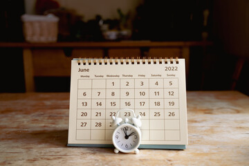 June 2022 calendar and little vintage white alarm clock on a wooden table