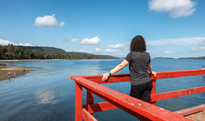 Fototapeta premium White Caucasian Woman on a Wooden Pier by the Pacific Ocean West Coast. Sunny Summer Day. Fernwood Point Beach, Salt Spring Island, British Columbia, Canada.
