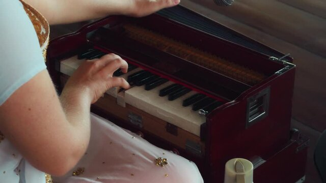 a girl sitting on a wooden floor and playing a keyboard ethnic Indian instrument