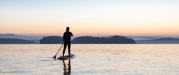Adventurous Caucasian Adult Woman on a Stand Up Paddle Board is paddling on the West Coast of...