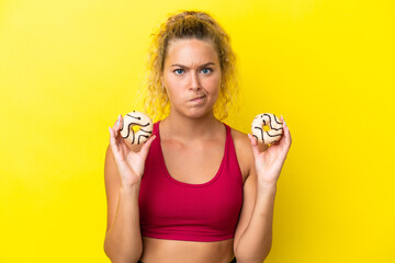 Girl with curly hair isolated on yellow background holding donuts with sad expression