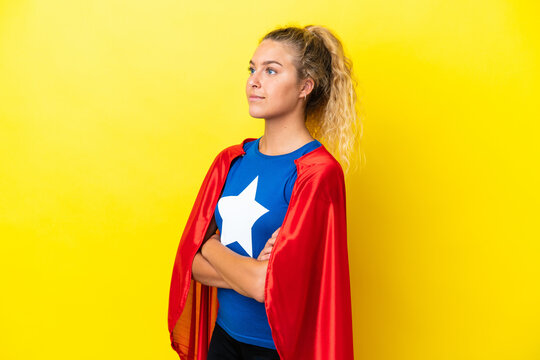 Girl with curly hair isolated on yellow background in superhero costume with arms crossed