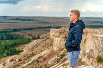 Naklejka na ściany i meble Handsome young blond man on a cliff overlooking the rustic landscape, White rock in Crimea